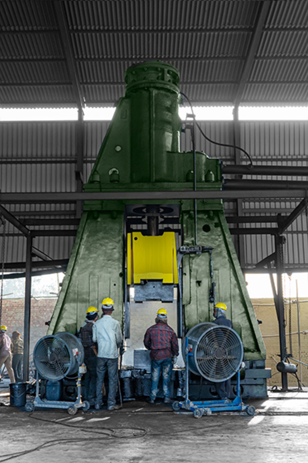 Operators in hard hats working at a green 10-ton pneumatic forging hammer inside the Bal Overseas forging shop