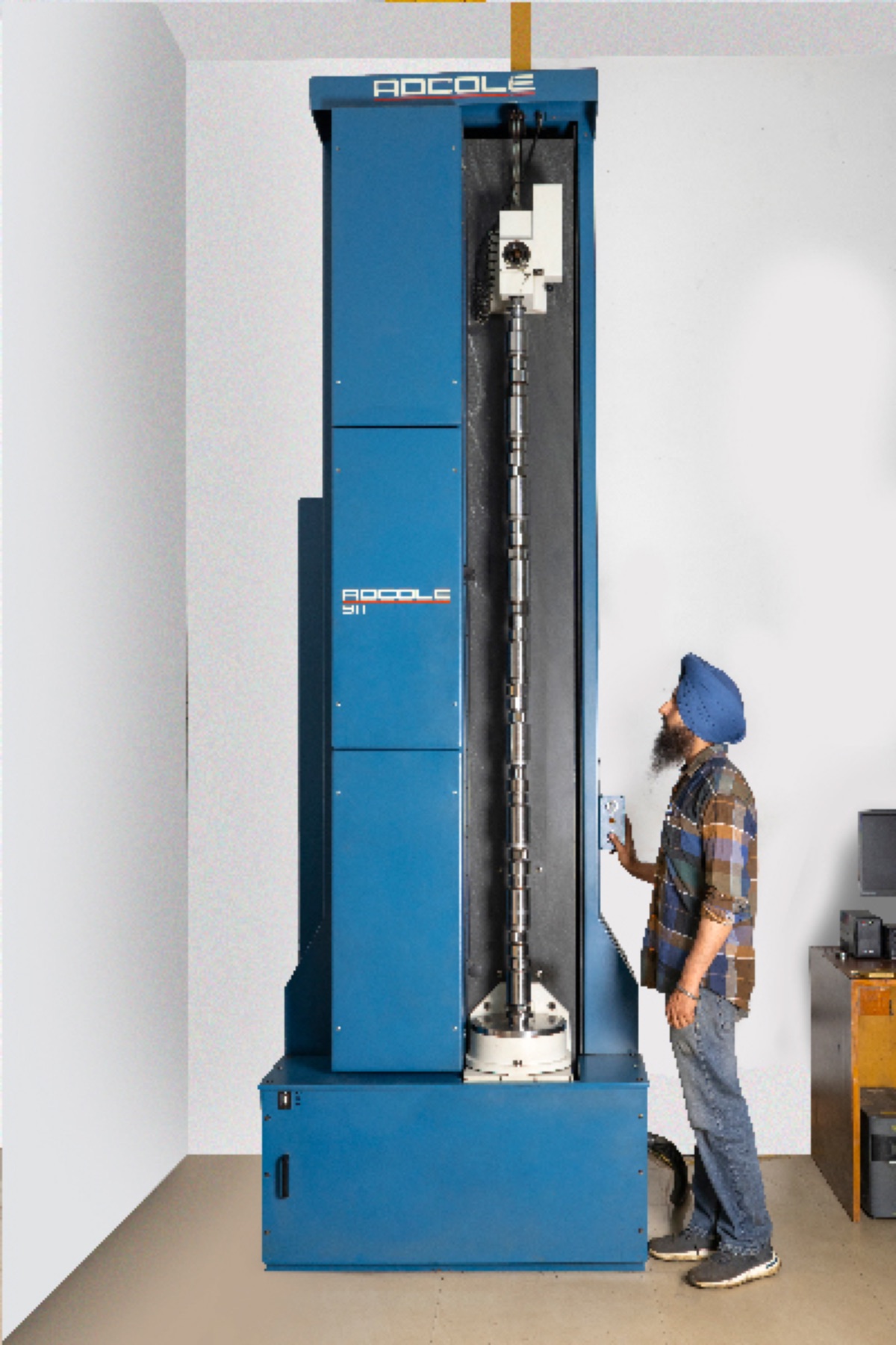 Engineer operating a blue Adcole 911 cam profile tester with a camshaft mounted vertically inside