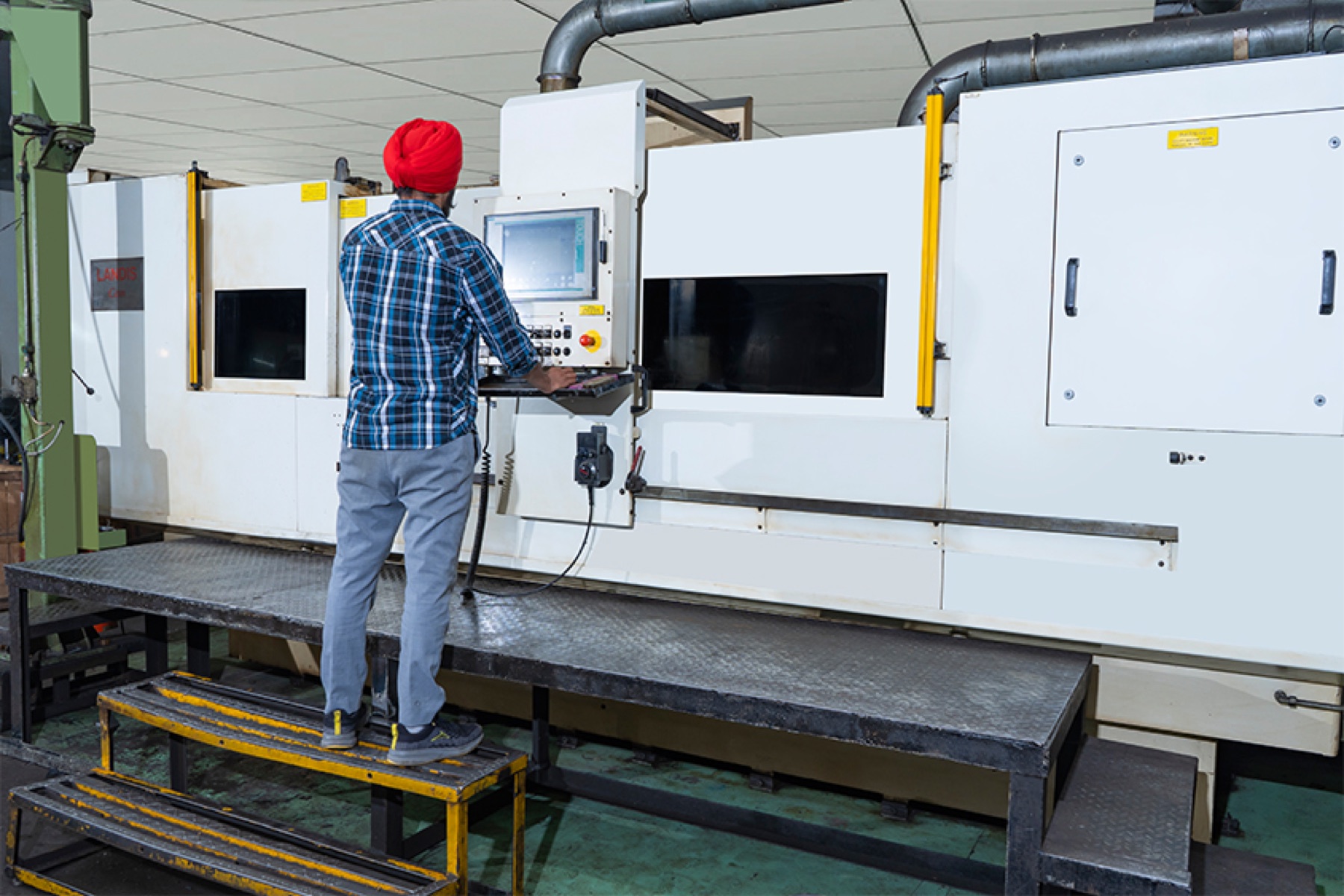 Operator running a LANDIS CNC cam grinding machine from a raised platform